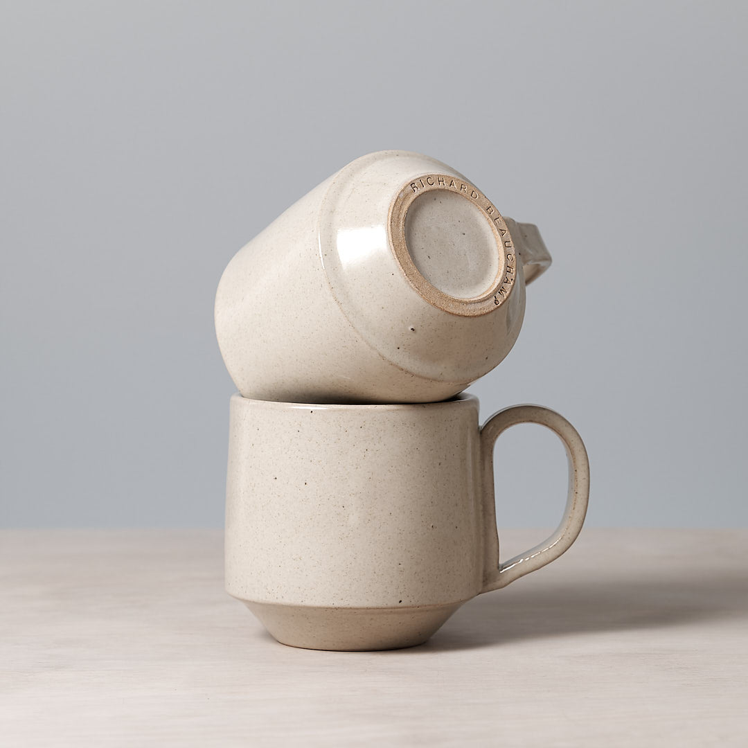 Two Large Stacking Mugs – Beige, made by Richard Beauchamp, stacked on top of each other on a table.