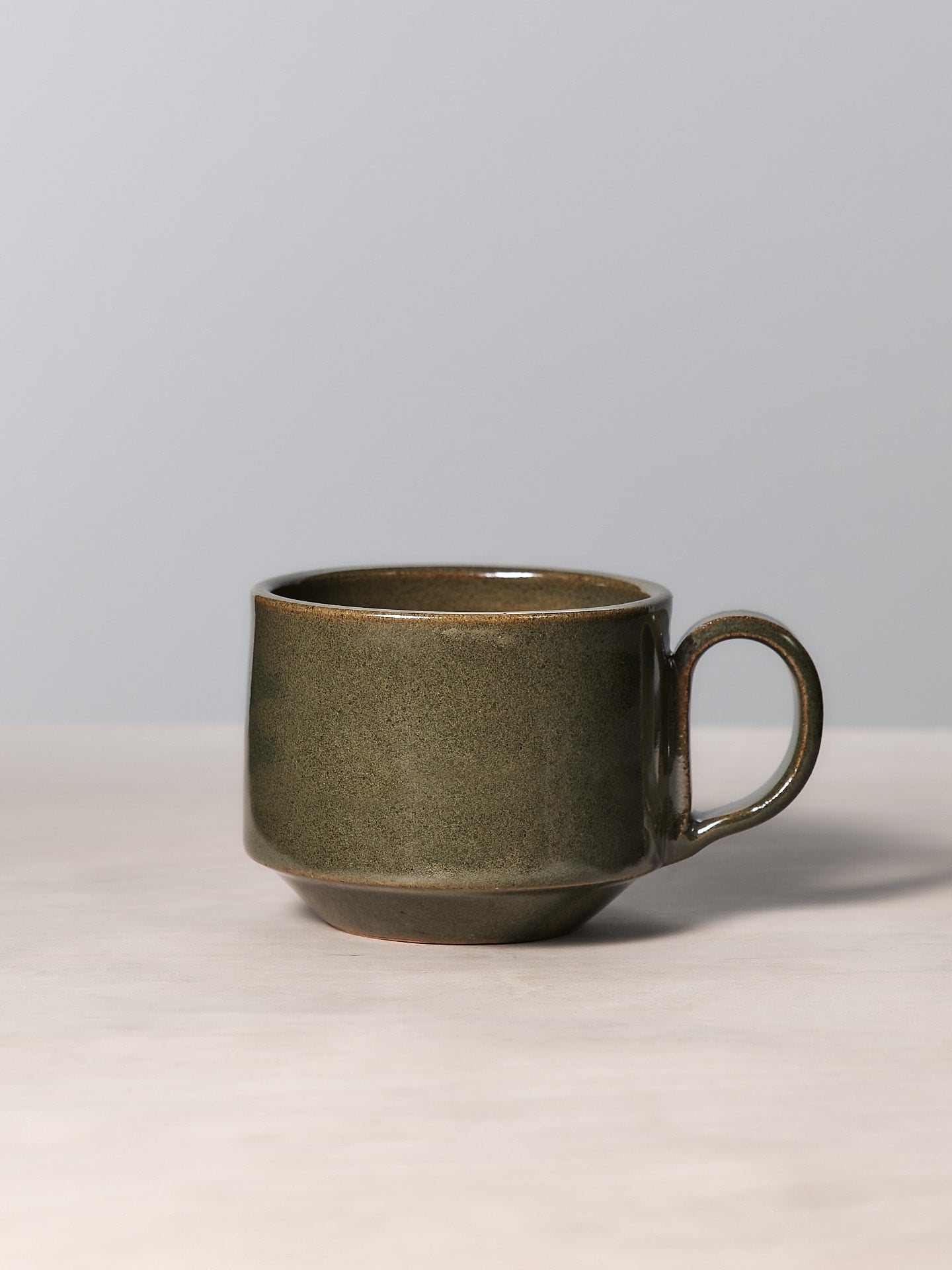 A Richard Beauchamp Medium Stacking Mug – Green with a green glaze sitting on a table in Ōtautahi Christchurch.