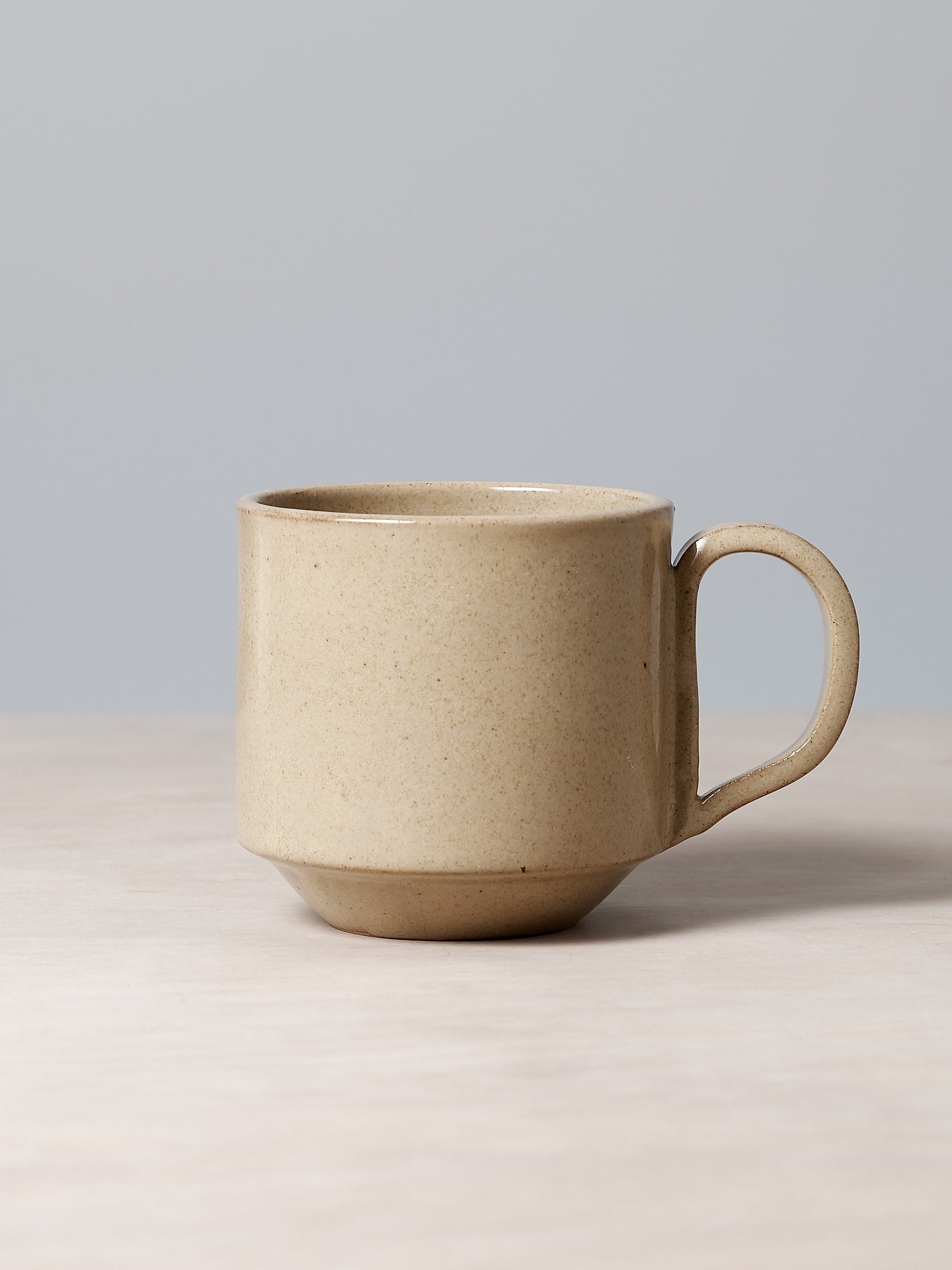 A Large Stacking Mug - Sand by Richard Beauchamp sitting on a wooden table.