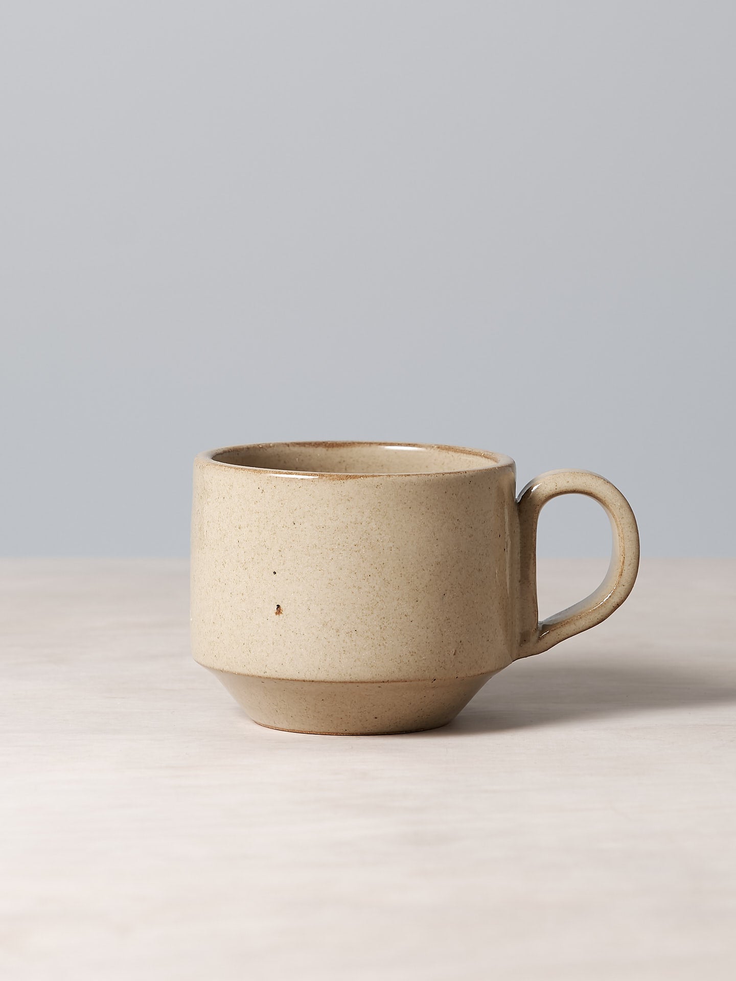 A Medium Stacking Mug – Sand from Richard Beauchamp sitting on a table.