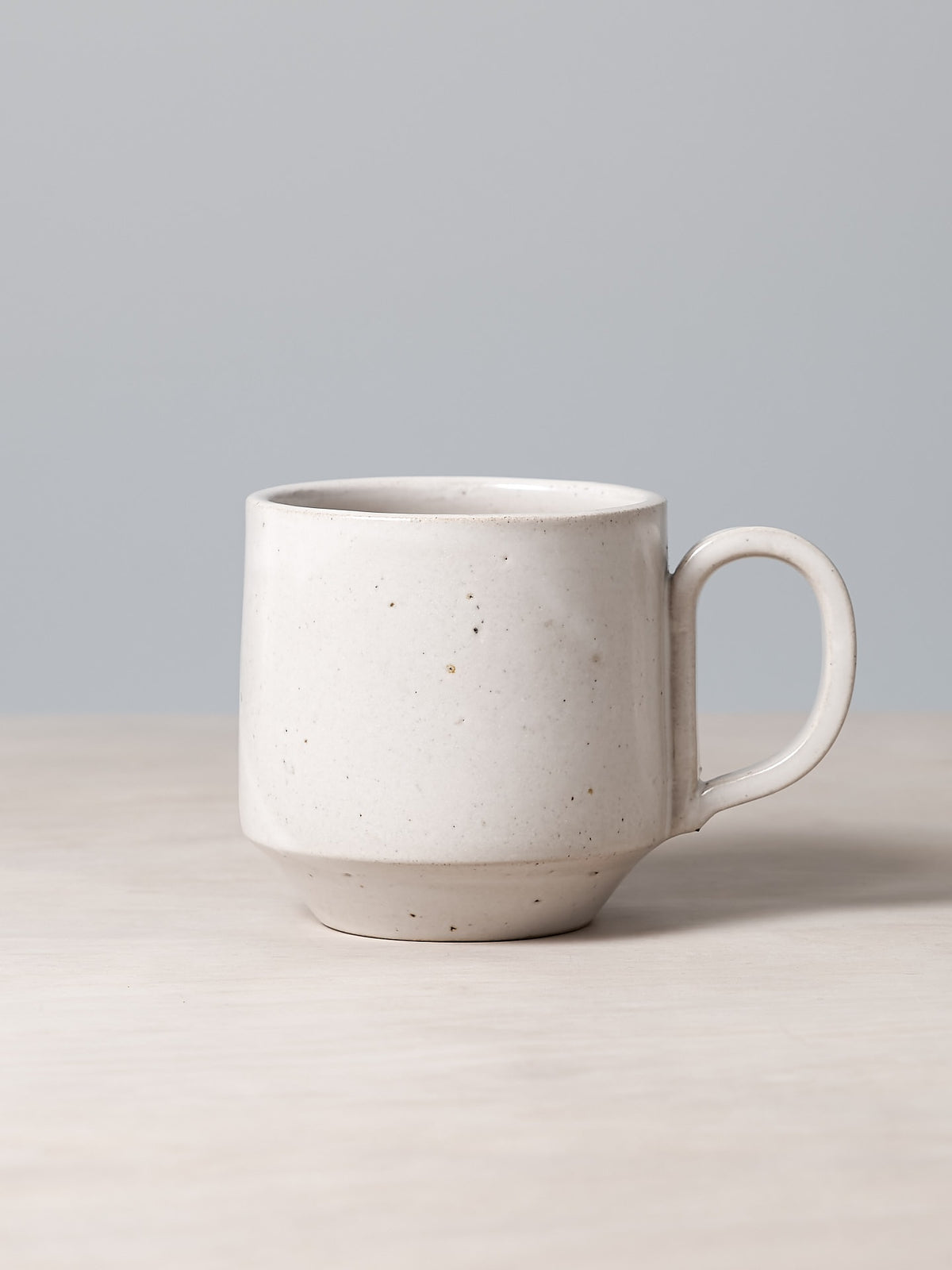 A Richard Beauchamp Tall Stacking Mug – White, rests elegantly on a wooden surface against a plain gray background, evoking the artisanal charm of Ōtautahi Christchurch.