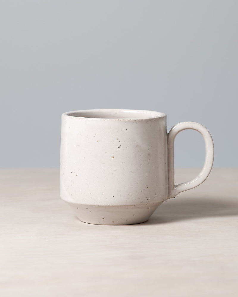 A Richard Beauchamp Tall Stacking Mug – White, rests elegantly on a wooden surface against a plain gray background, evoking the artisanal charm of Ōtautahi Christchurch.