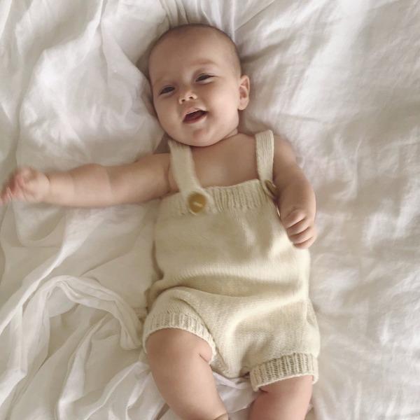 A baby is laying on a bed in a Weebits Hand Knitted Romper - Natural.