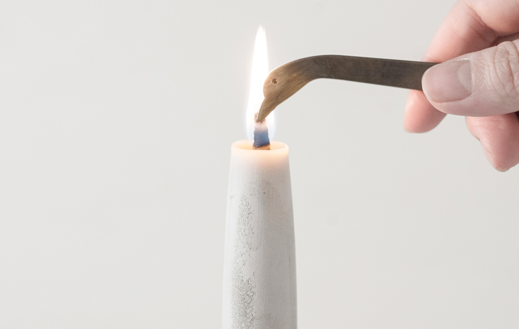 A person lighting a TOHAKU candle with a metal tweezers.