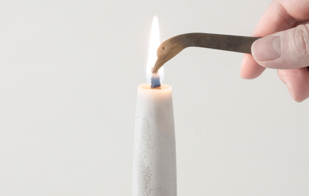 A person delicately lighting a Takazawa TOHAKU – Small (8 piece box set) candle using metal tweezers.