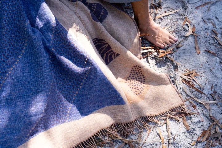 A person laying on a Seljak Brand Gather Blanket in the sand.