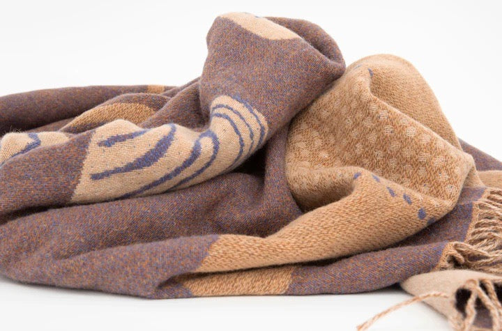 A Gather Blanket by Seljak Brand, brown and tan, on a white surface.