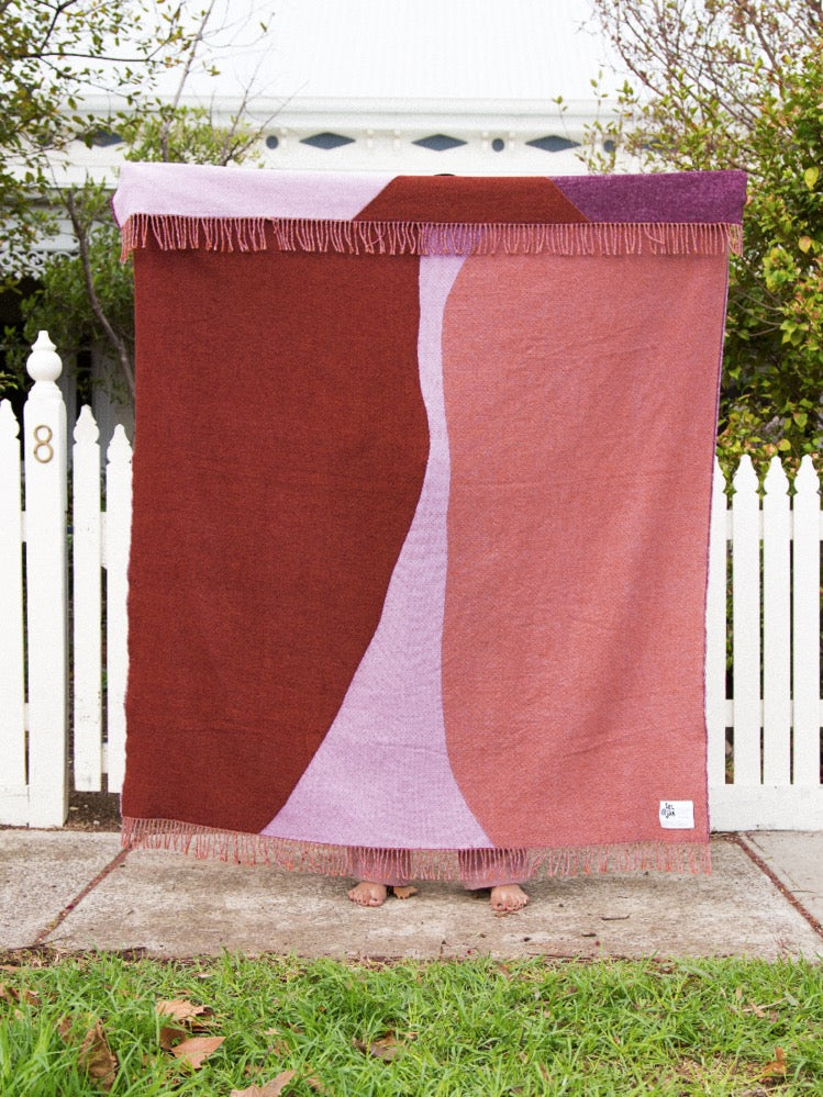 A person holding a Seljak Brand Dune Blanket in front of a white picket fence.