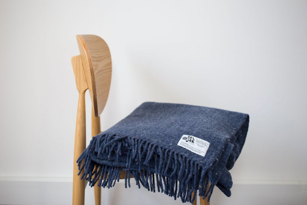 An Indigo Blanket – Fringe by Seljak Brand on a wooden chair.