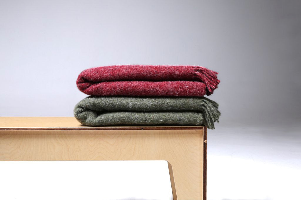 A Moss Blanket – Fringe by Seljak Brand is sitting on a wooden bench.