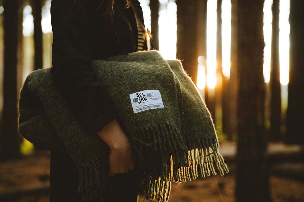 A woman holding a Moss Blanket – Fringe by Seljak Brand in the woods.