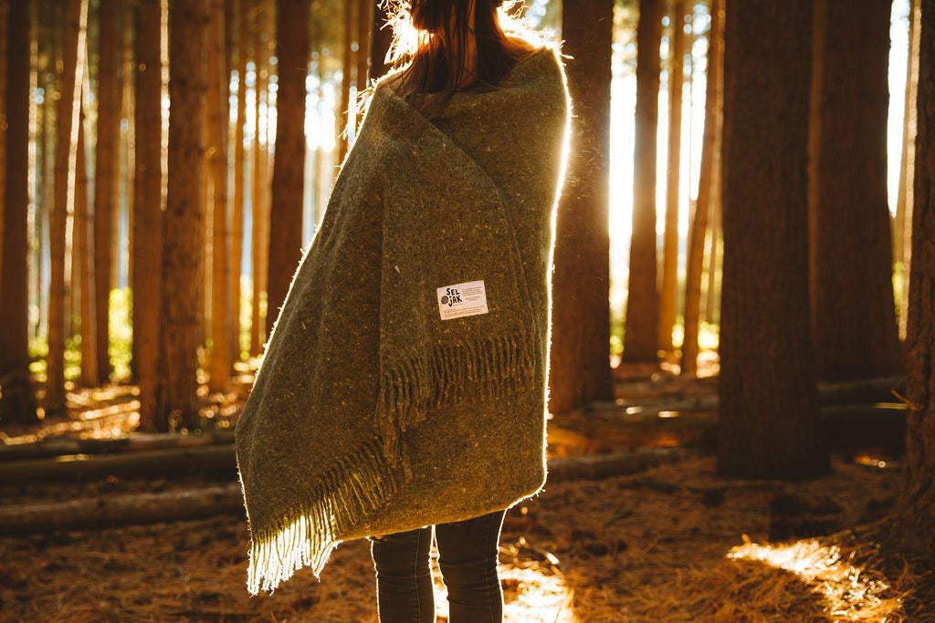 A woman standing in the woods wearing a Moss Blanket – Fringe by Seljak Brand.