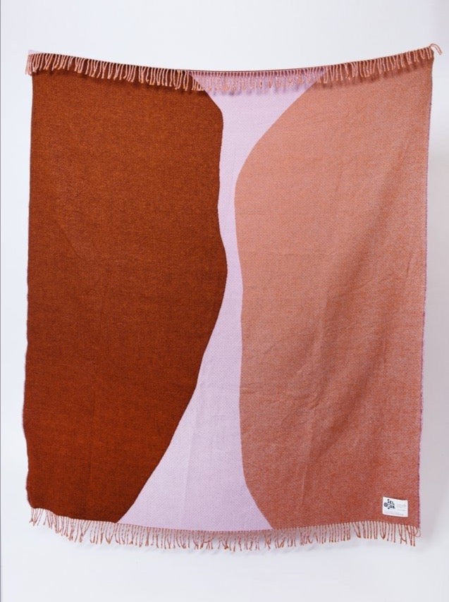 A brown and pink Dune Blanket hanging on a white wall by Seljak Brand.