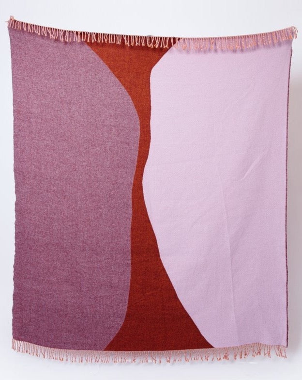 A pink and brown Dune Blanket by Seljak Brand hanging on a wall.