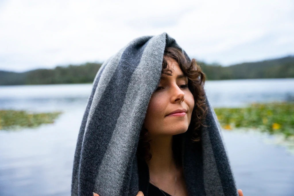 A woman wrapped in a Moontide Blanket near a lake. (Brand: Seljak Brand)