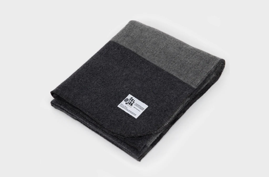 A grey and black Moontide Blanket by Seljak Brand on a white surface.