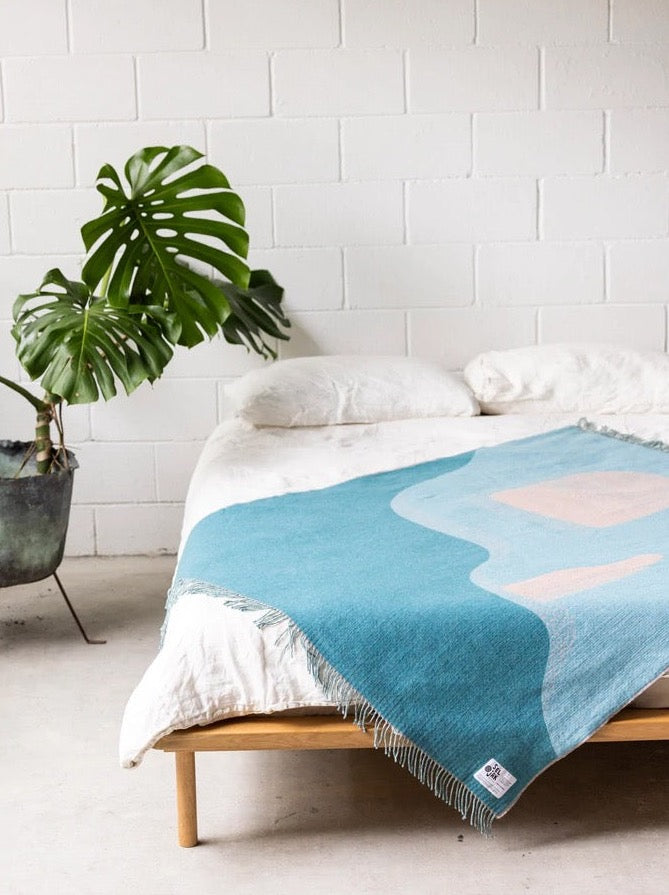 A bed with a Passage Blanket and a plant on it.