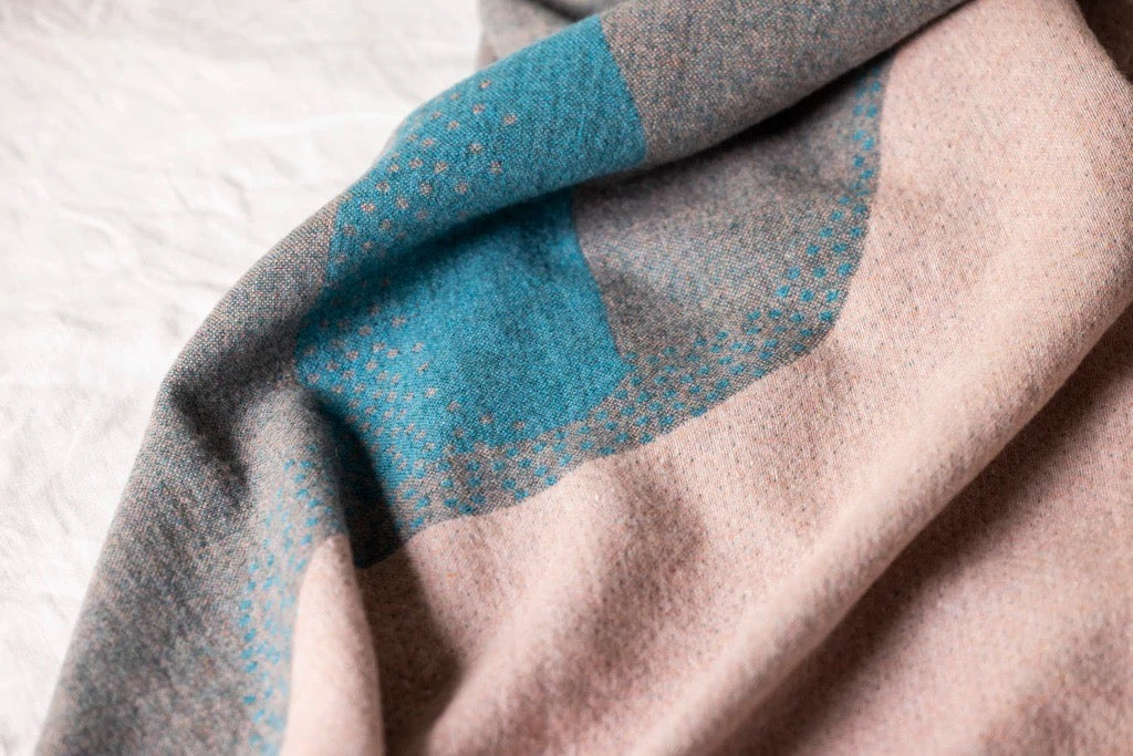 A Passage Blanket with blue and pink stripes on it by Seljak Brand.