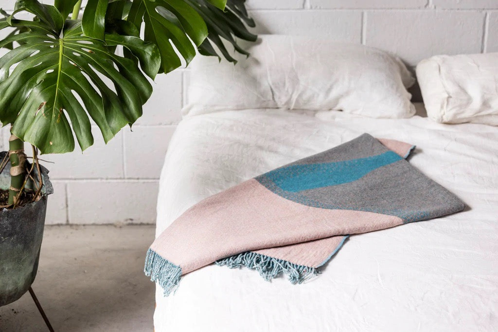 A bed with a Seljak brand Passage Blanket and a plant on it.