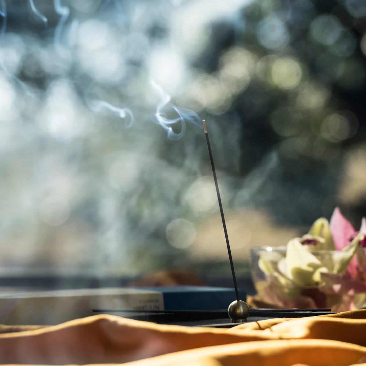 A Senko Brass Ball Incense Holder on a table with flowers.
