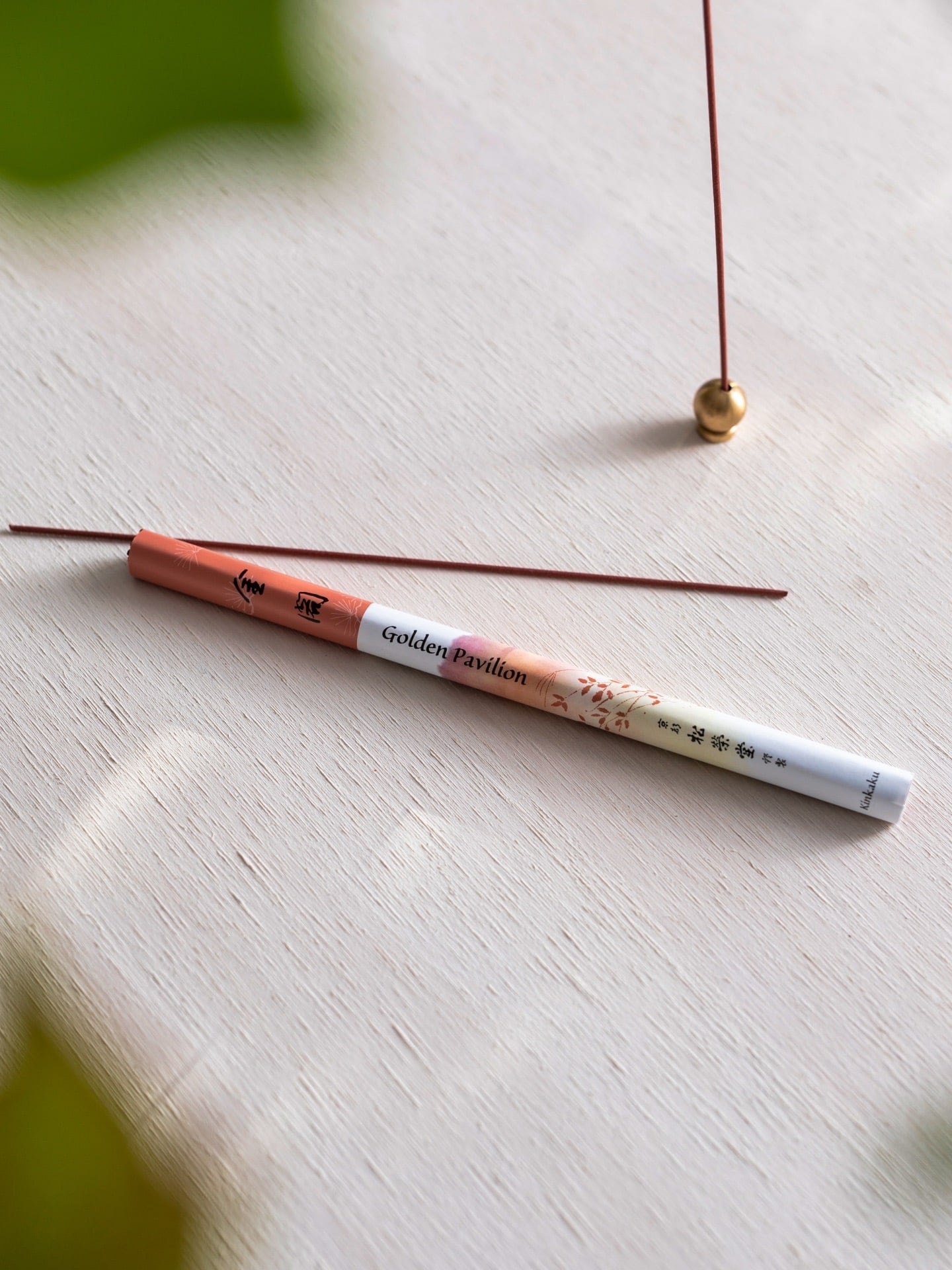 A Senko incense stick on a table next to a plant, called Golden Pavilion - Kinkaku.