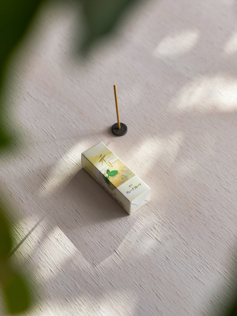 An Grapefruit with Holder – Xiang Do incense stick on top of a wooden table.