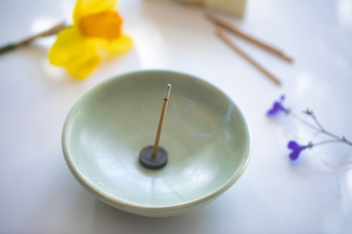 A Grapefruit with Holder – Xiang Do incense stick in a bowl next to flowers.