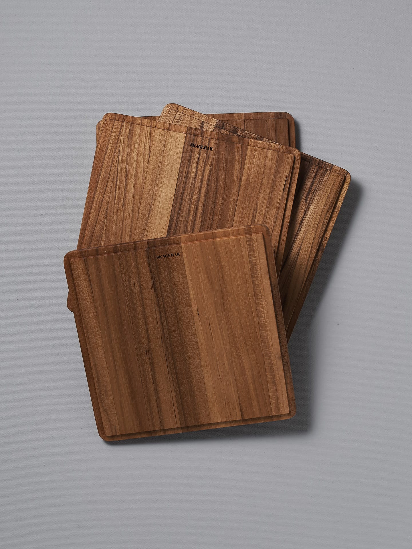 Four Skagerak Plank Square Trencher 4pcs – Teak cutting boards on a grey surface.