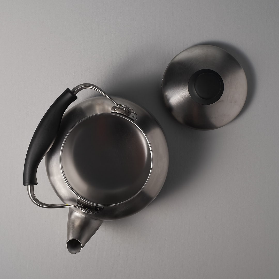 A Stove-top Kettle – Brushed Steel with a lid on a gray surface. (Brand Name: Sori Yanagi)