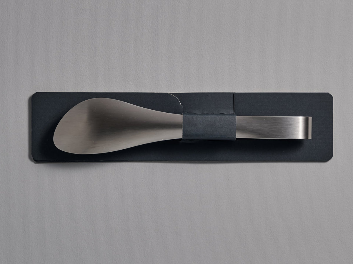 A Sori Yanagi silver tong with a black handle on a gray wall.