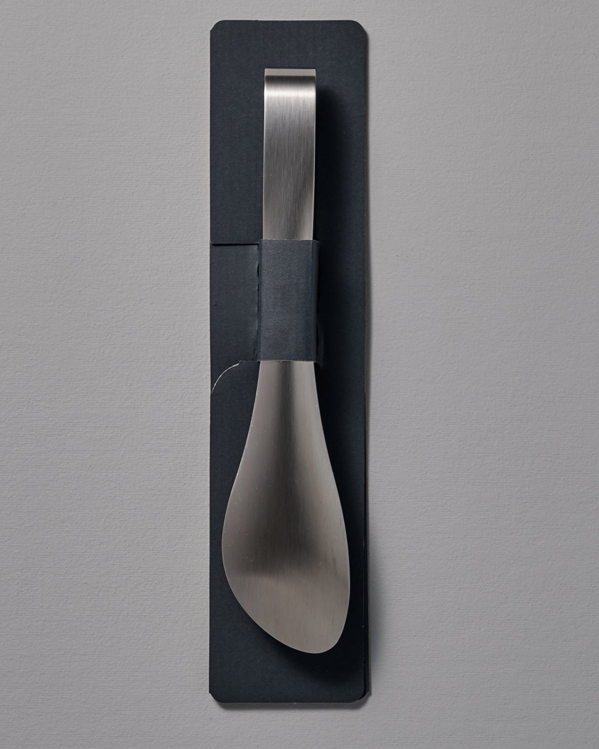 A Sori Yanagi silver tong with a black handle on a gray wall.