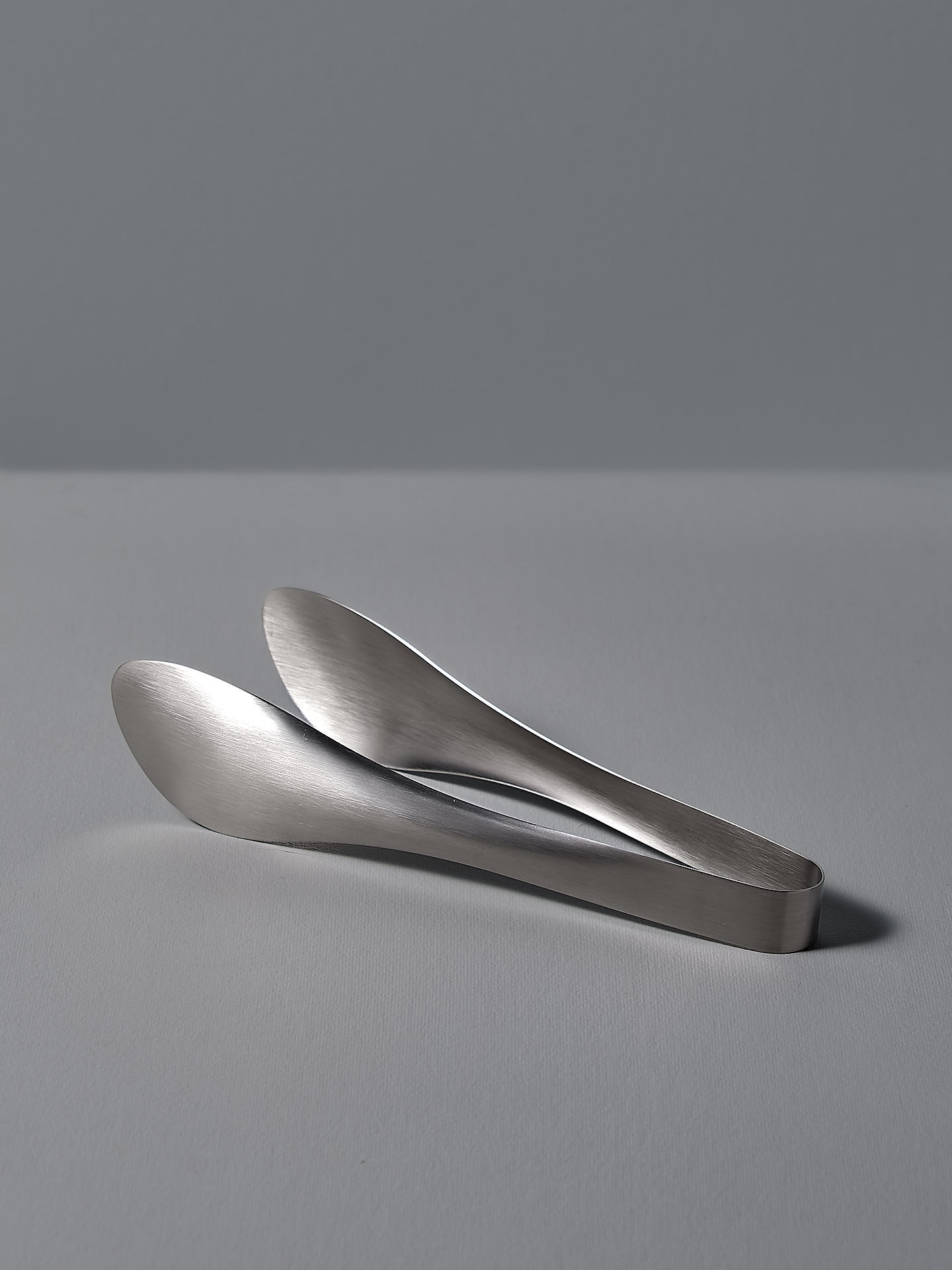 A pair of Sori Yanagi tongs on a white surface.