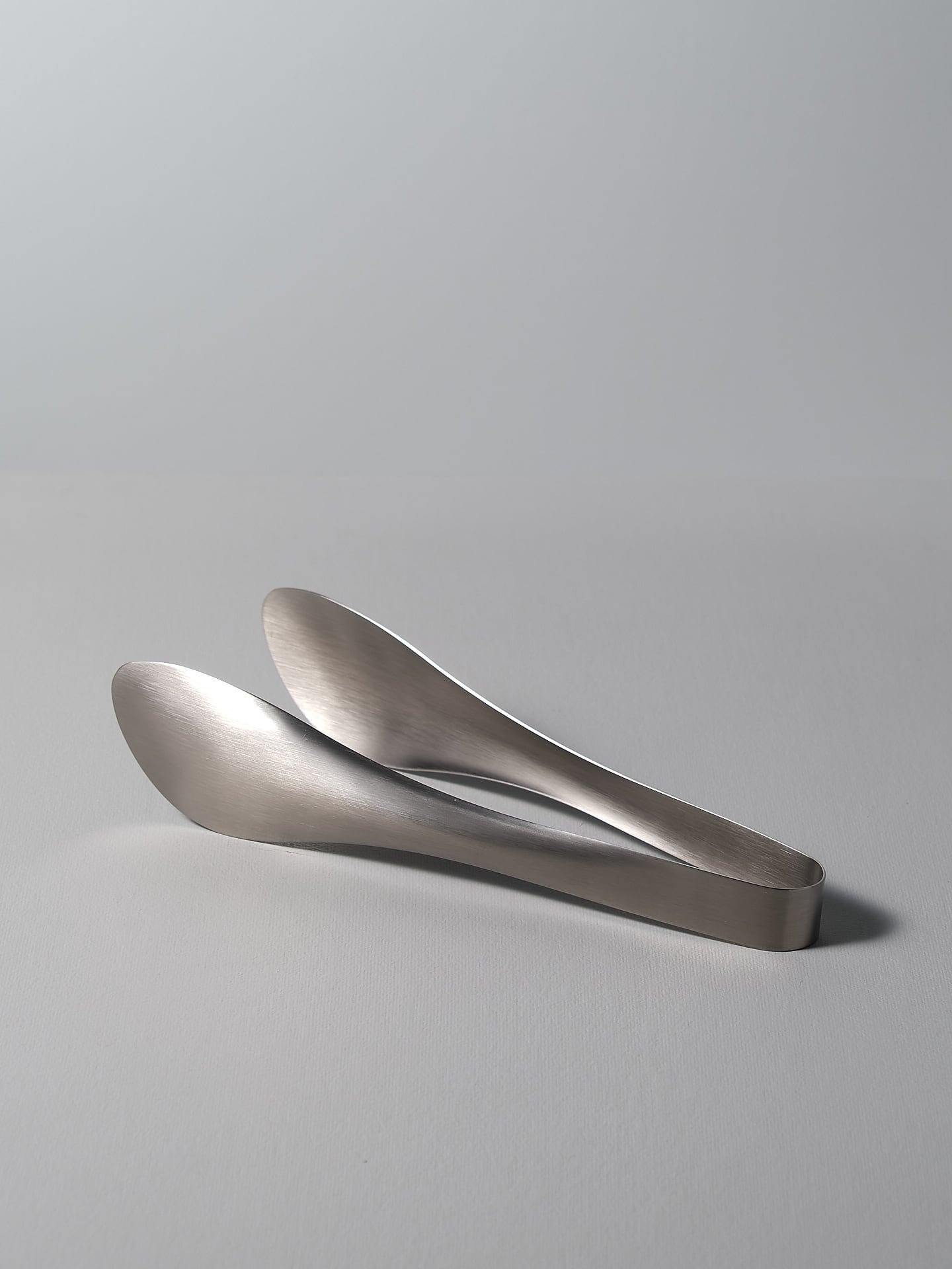 A pair of Sori Yanagi tongs on a white surface.