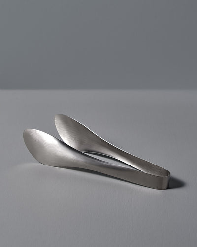 A pair of Sori Yanagi tongs on a white surface.