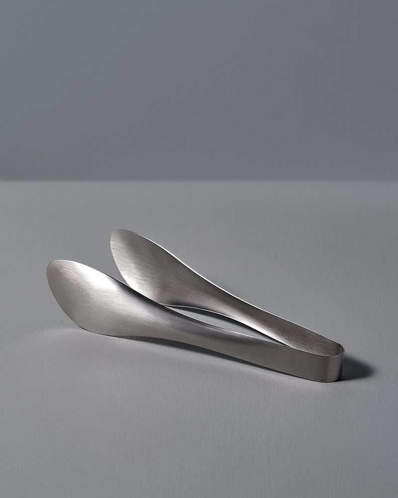 A pair of Sori Yanagi tongs on a white surface.