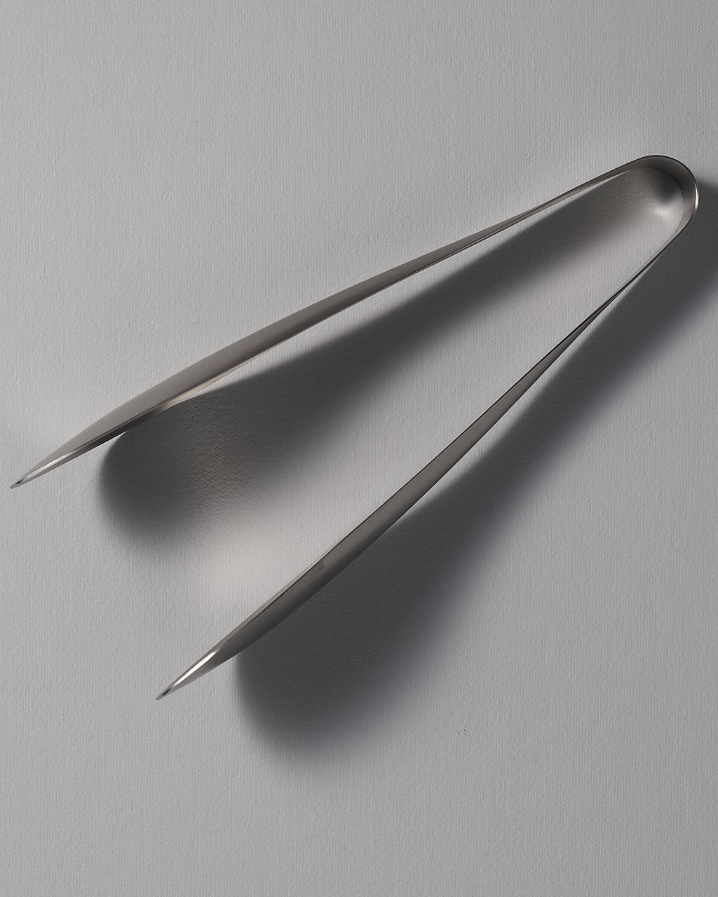 A pair of Sori Yanagi tongs on a white surface.