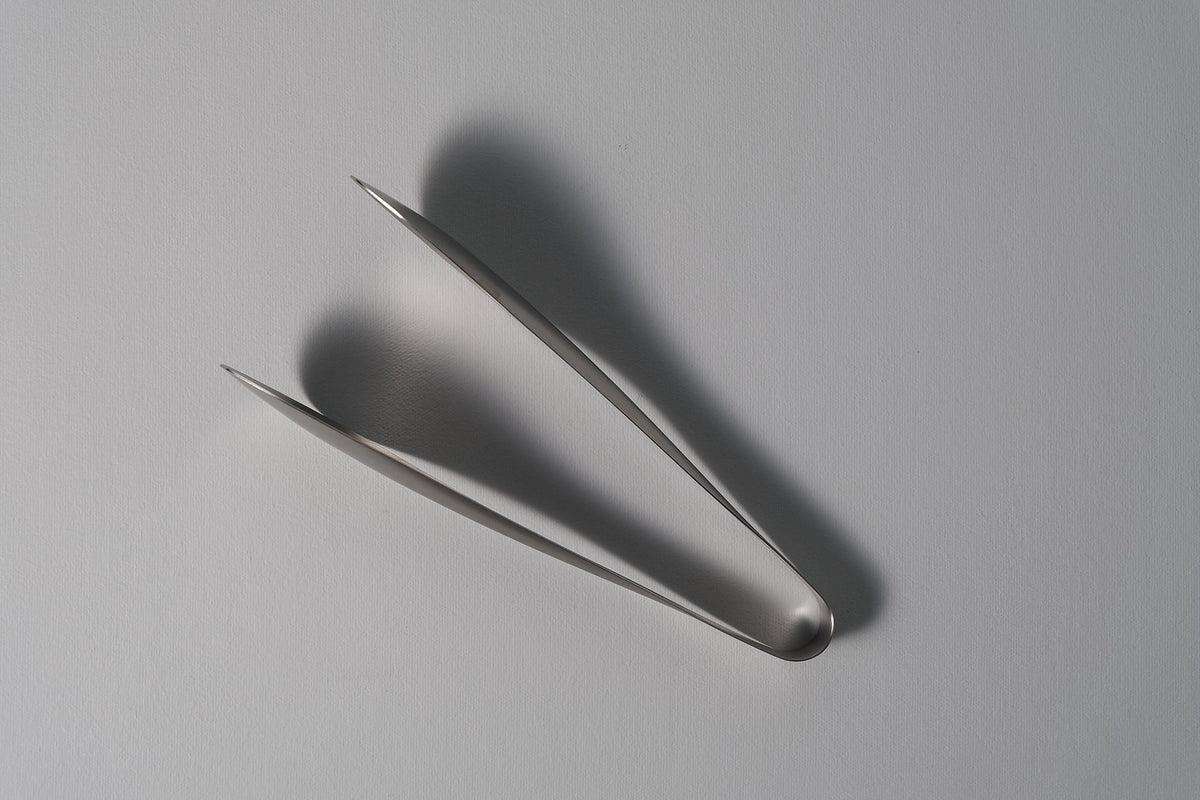 A pair of Sori Yanagi tongs on a white surface.
