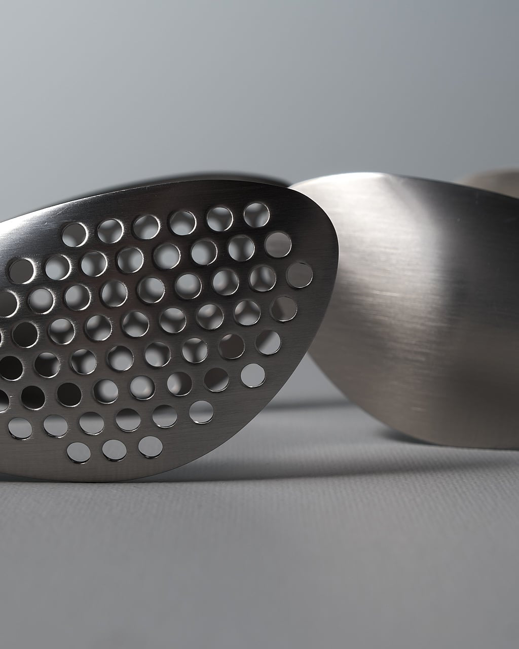 A pair of Sori Yanagi stainless steel tongs - perforated on a white surface.