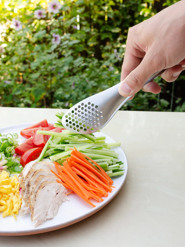 A person using Sori Yanagi&#39;s Perforated Tongs to grate vegetables on a plate.