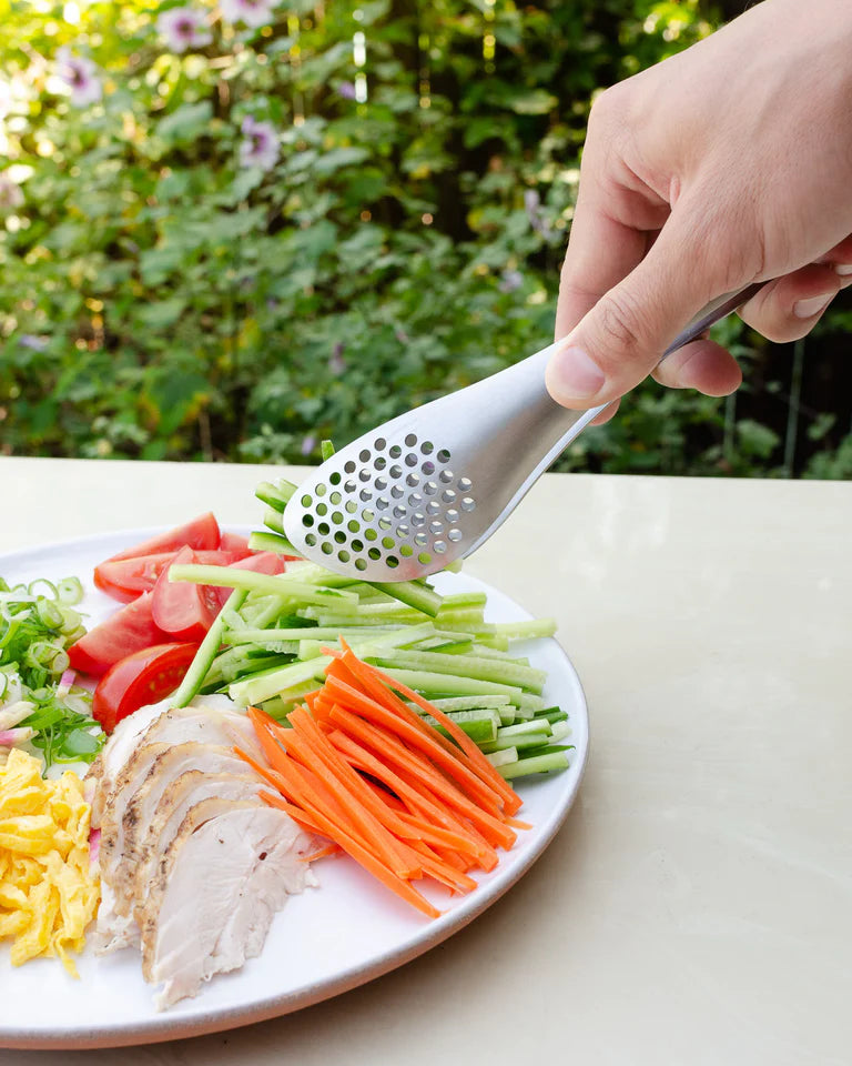 A person using Sori Yanagi's Perforated Tongs to grate vegetables on a plate.