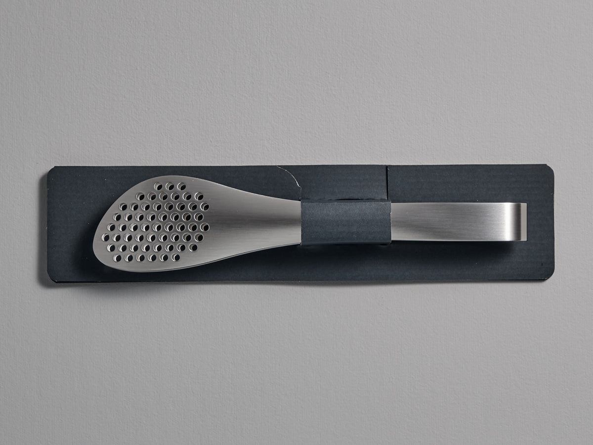 A Sori Yanagi stainless steel Tongs - Perforated utensil holder on a gray wall.