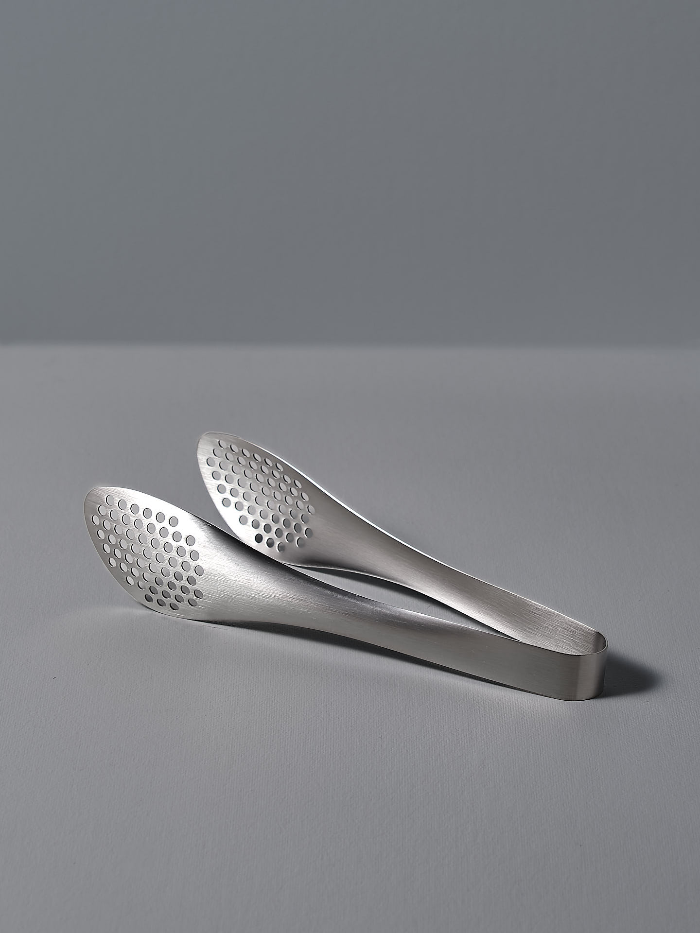 A pair of Sori Yanagi stainless steel tongs - perforated on a white surface.