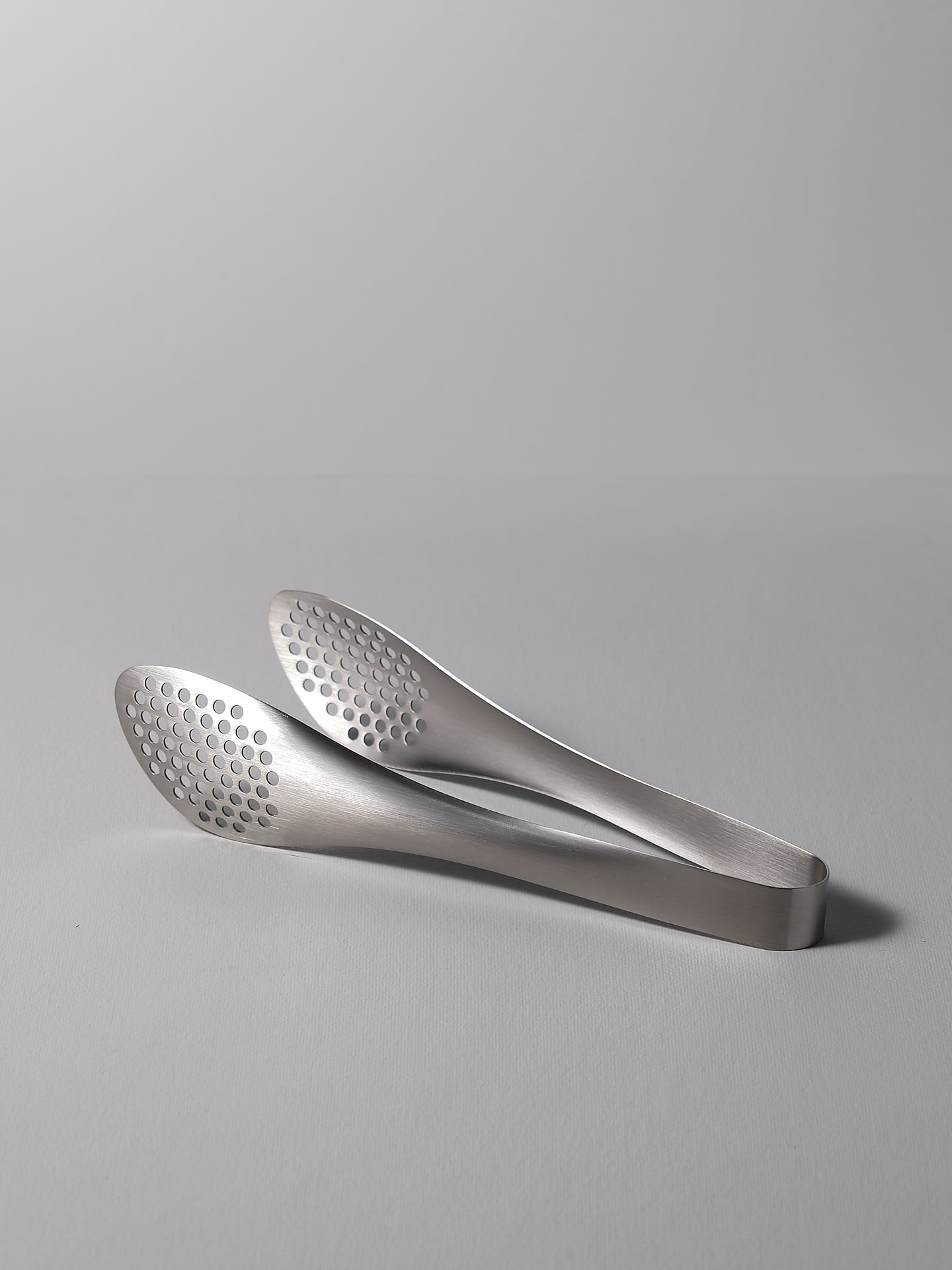 A pair of Sori Yanagi stainless steel tongs - perforated on a white surface.