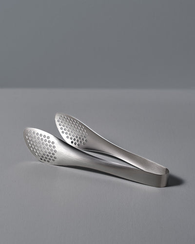 A pair of Sori Yanagi stainless steel tongs - perforated on a white surface.