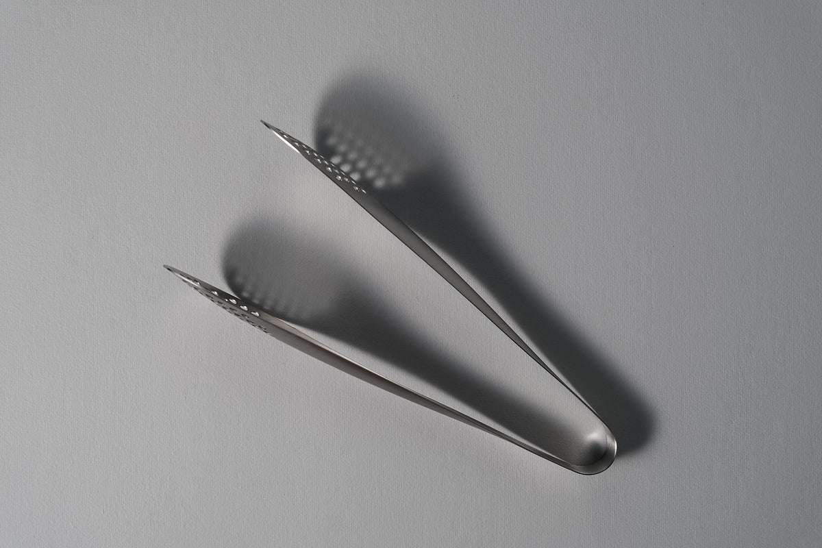A pair of Sori Yanagi tongs (perforated) on a white surface.