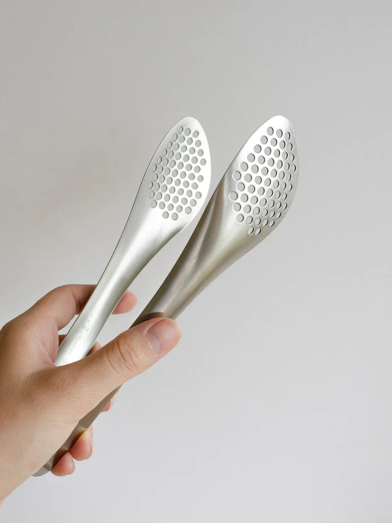 A person holding a pair of Sori Yanagi stainless steel tongs – perforated.
