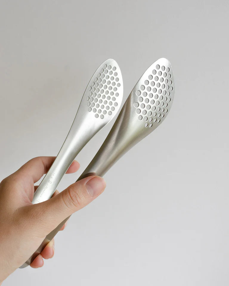 A person holding a pair of Sori Yanagi stainless steel tongs – perforated.