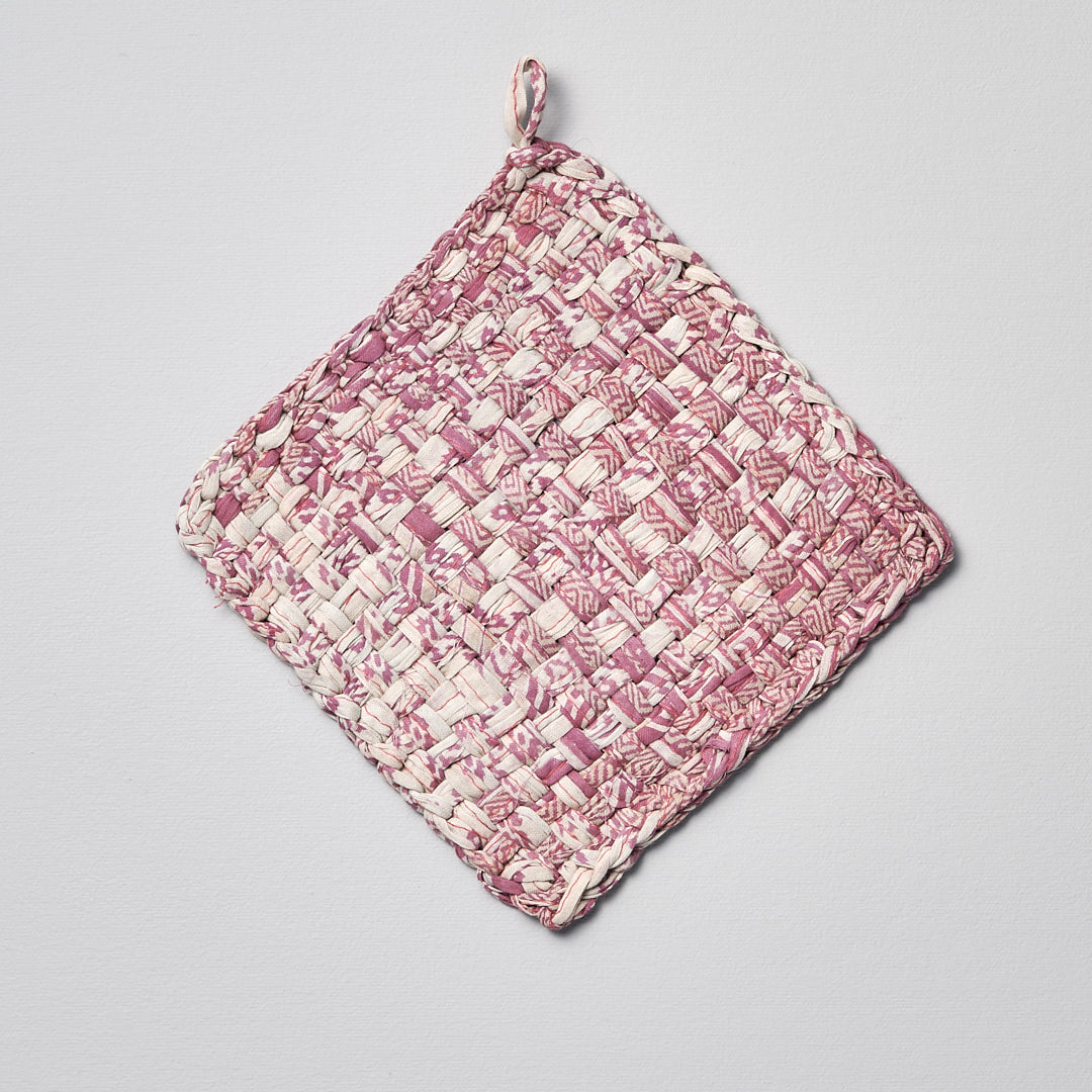 A pink and white Sari Pot &amp; Oven-tray Holder by Stitchwallah hanging on a white surface.