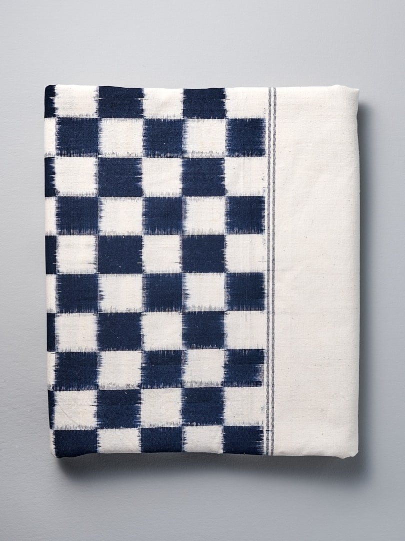 An Ikat Weave Tablecloth – Indigo Check by Stitchwallah on a white surface.