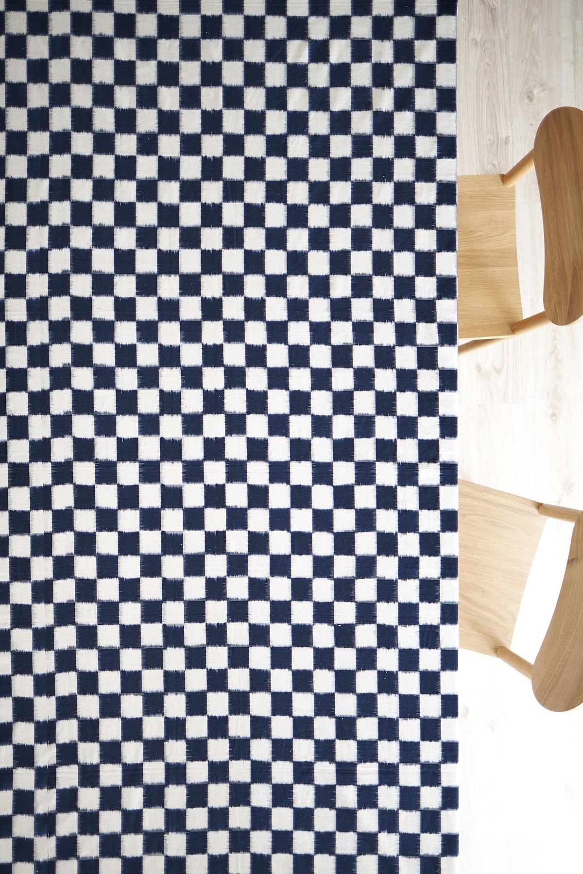 A Ikat Weave Tablecloth – Indigo Check by Stitchwallah on a wooden floor.